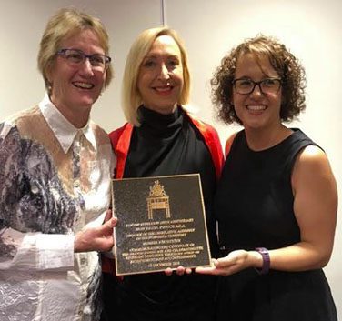 Three women holding plaque.